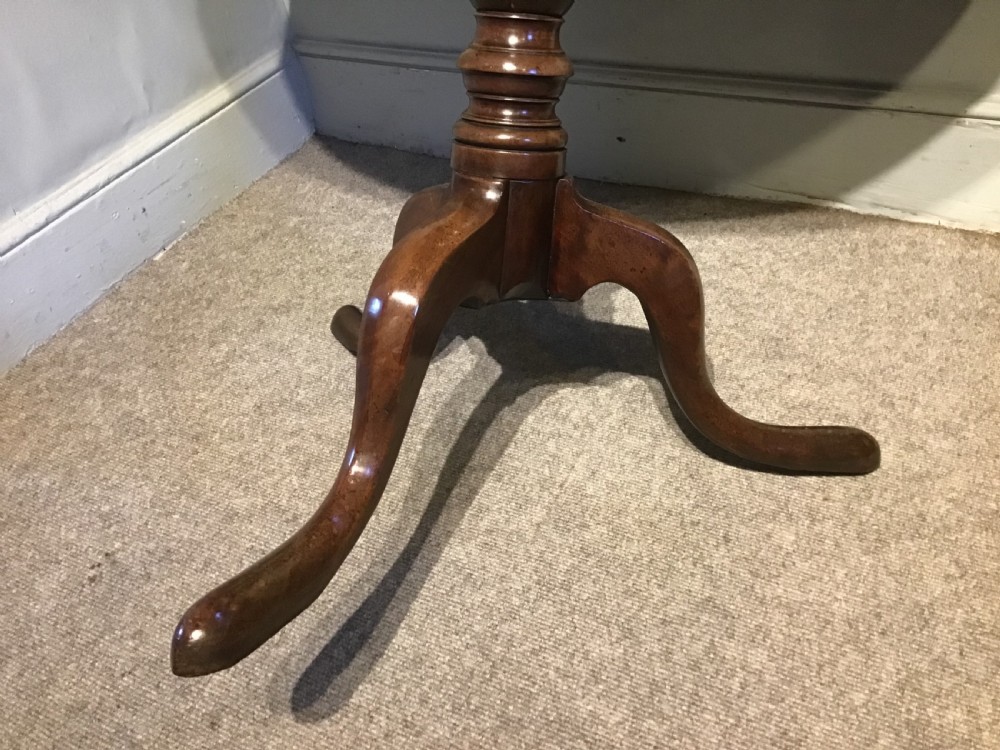 A Georgian mahogany tripod table with a circular tilt-top raised on a turned central pedestal and three cabriole legs. View V