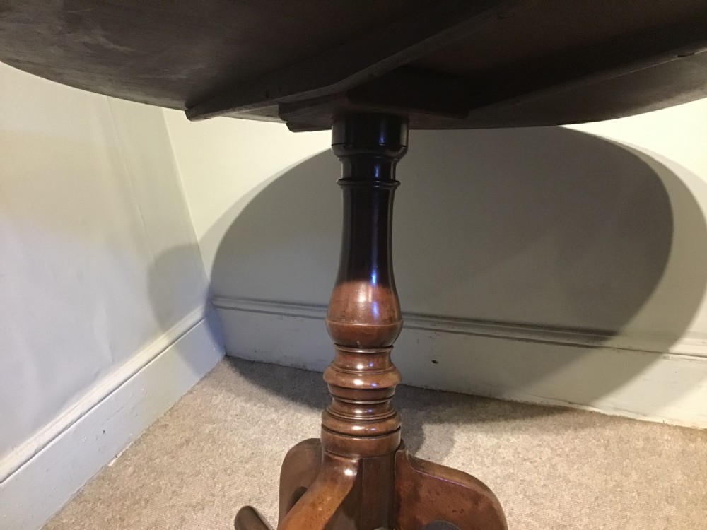 A Georgian mahogany tripod table with a circular tilt-top raised on a turned central pedestal and three cabriole legs. View VI