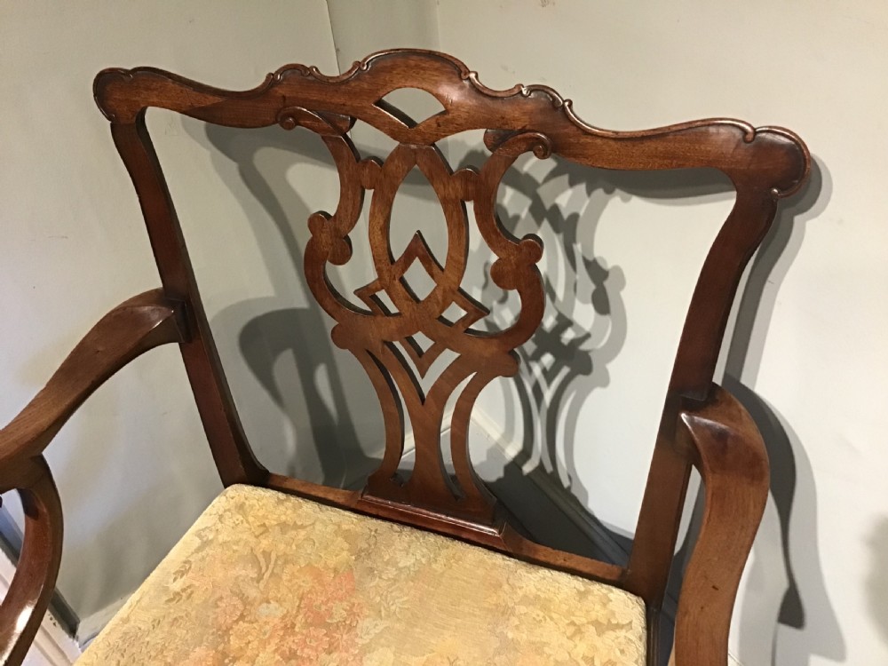An antique mahogany elbow chair featuring a carved pierced back splat, curved arms, and a soft beige floral tapestry seat. View III