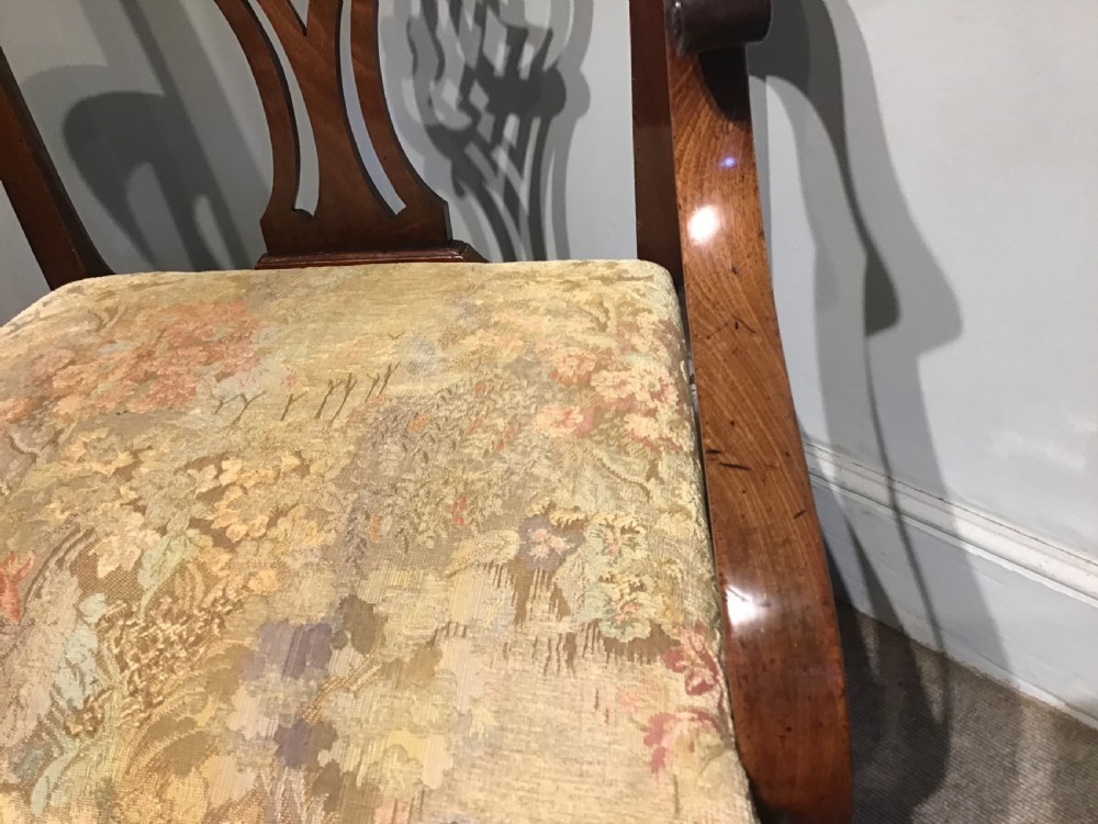 An antique mahogany elbow chair featuring a carved pierced back splat, curved arms, and a soft beige floral tapestry seat. View IV