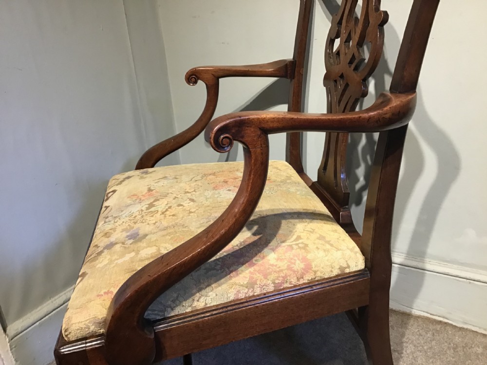 An antique mahogany elbow chair featuring a carved pierced back splat, curved arms, and a soft beige floral tapestry seat. View VII