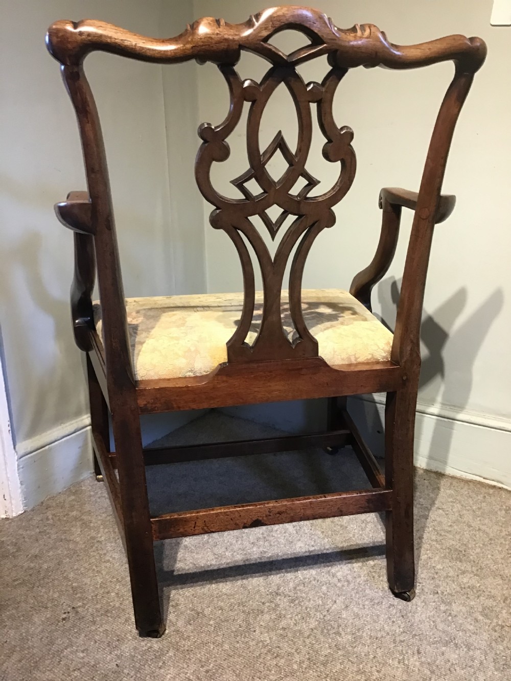 An antique mahogany elbow chair featuring a carved pierced back splat, curved arms, and a soft beige floral tapestry seat. View VIII
