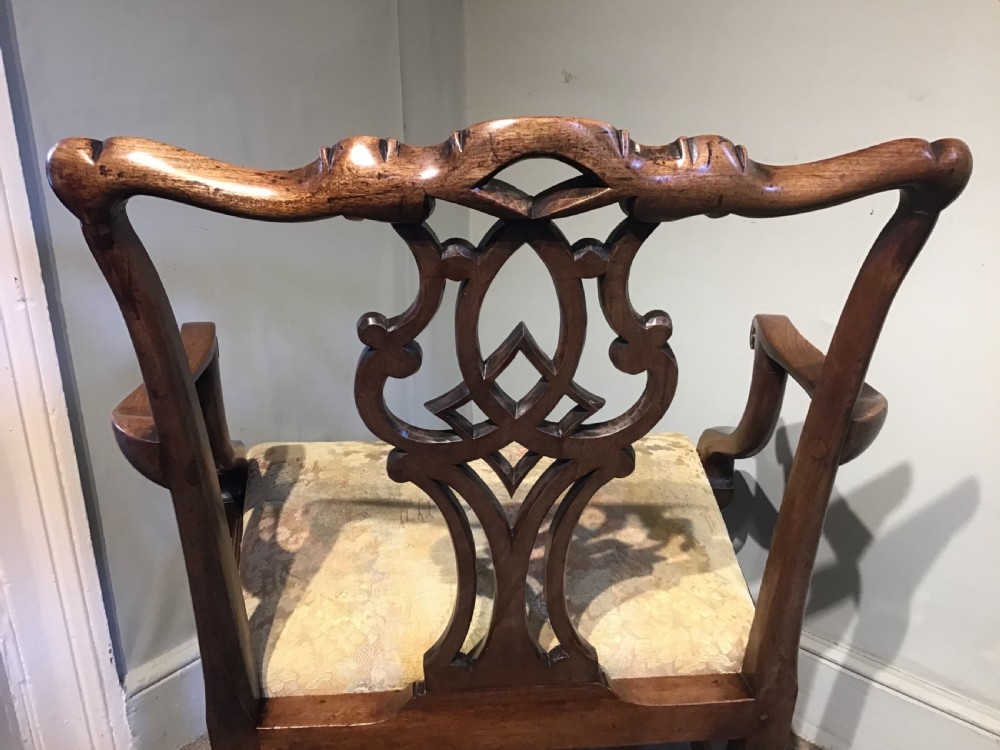 An antique mahogany elbow chair featuring a carved pierced back splat, curved arms, and a soft beige floral tapestry seat. View IX