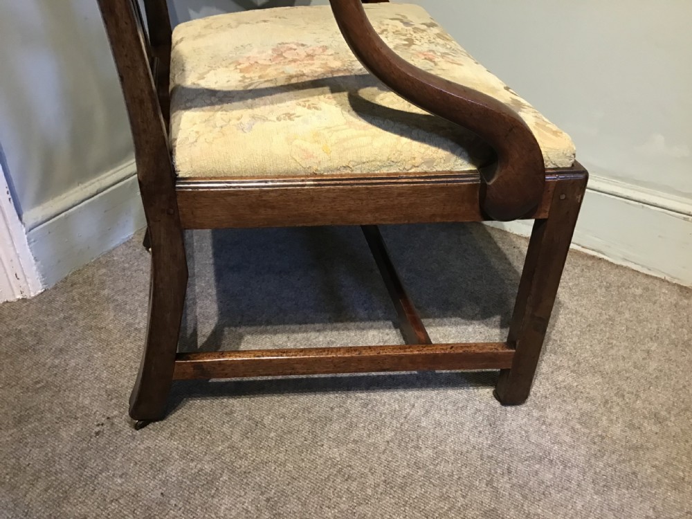 An antique mahogany elbow chair featuring a carved pierced back splat, curved arms, and a soft beige floral tapestry seat. View X