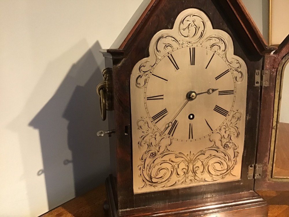 An antique mahogany bracket clock featuring a pointed gabled top, side brass ring handles, ball feet, and an engraved metal dial with Roman numerals. View III