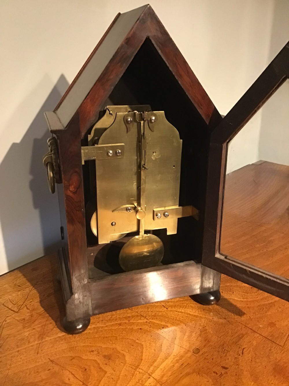 An antique mahogany bracket clock featuring a pointed gabled top, side brass ring handles, ball feet, and an engraved metal dial with Roman numerals. View VIII