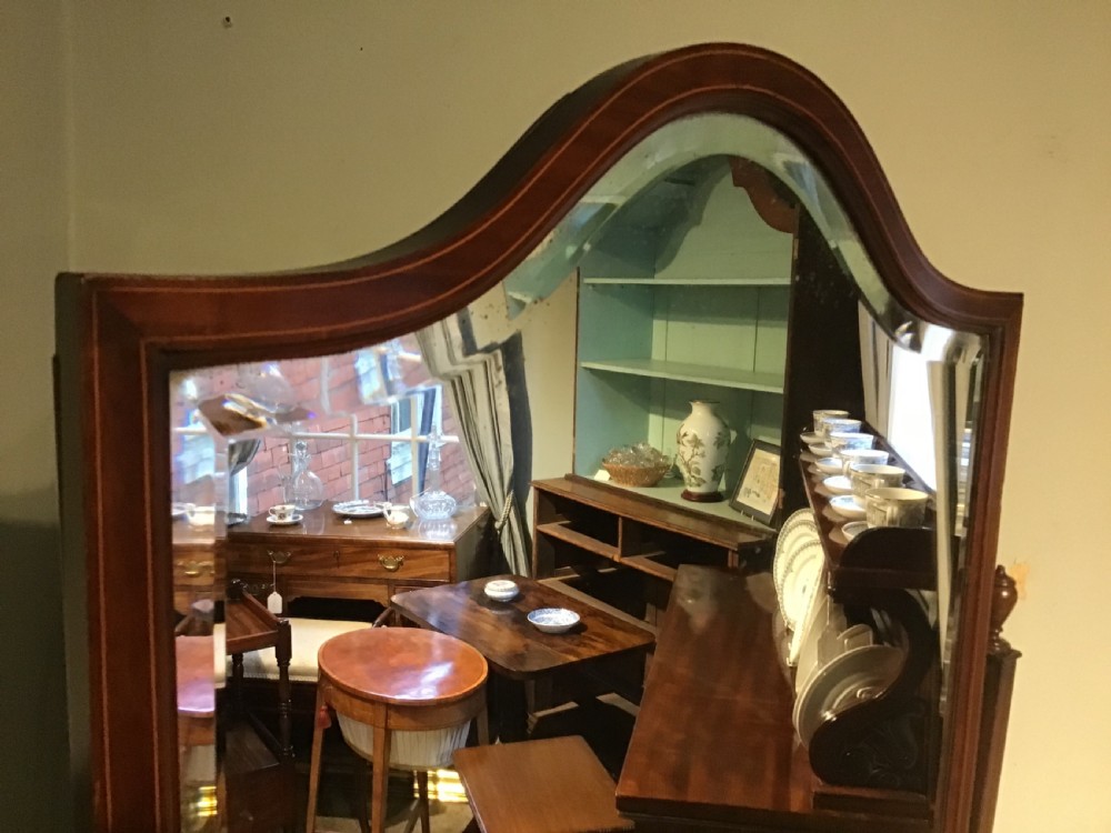 An antique mahogany cheval mirror featuring a shield-shaped tilting glass frame supported by curved uprights on splayed legs with brass castors. View II