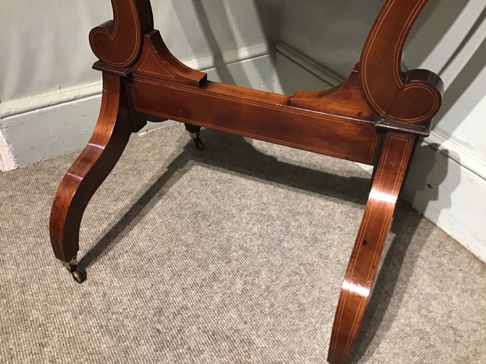 An antique mahogany cheval mirror featuring a shield-shaped tilting glass frame supported by curved uprights on splayed legs with brass castors. View V