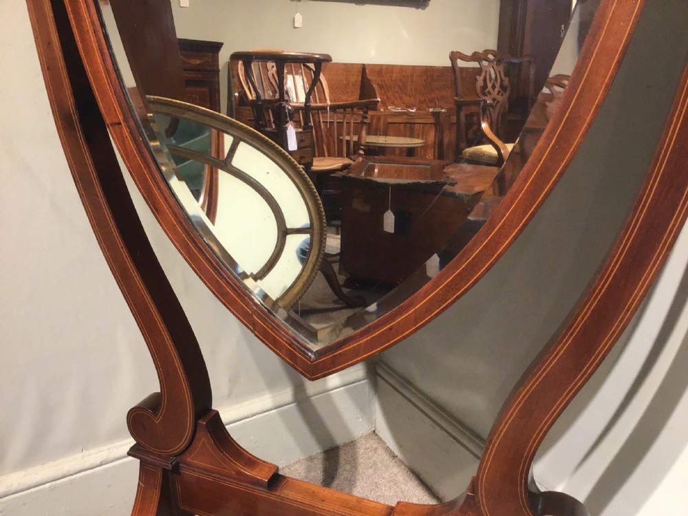 An antique mahogany cheval mirror featuring a shield-shaped tilting glass frame supported by curved uprights on splayed legs with brass castors. View VI