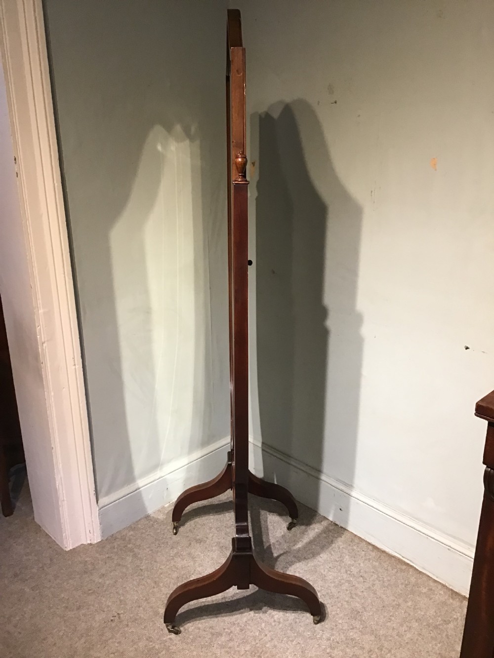 An antique mahogany cheval mirror featuring a shield-shaped tilting glass frame supported by curved uprights on splayed legs with brass castors. View VIII
