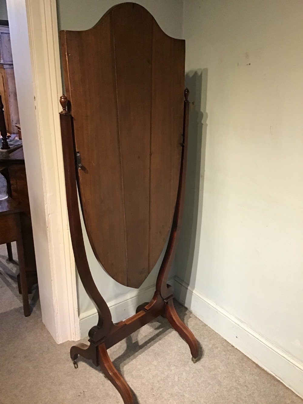 An antique mahogany cheval mirror featuring a shield-shaped tilting glass frame supported by curved uprights on splayed legs with brass castors. View IX
