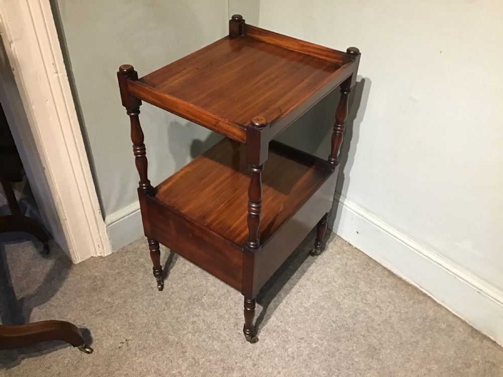 A warm brown mahogany tiered side table with turned supports, a gallery top, an open shelf, a lower drawer with brass knobs, and brass castors. View V