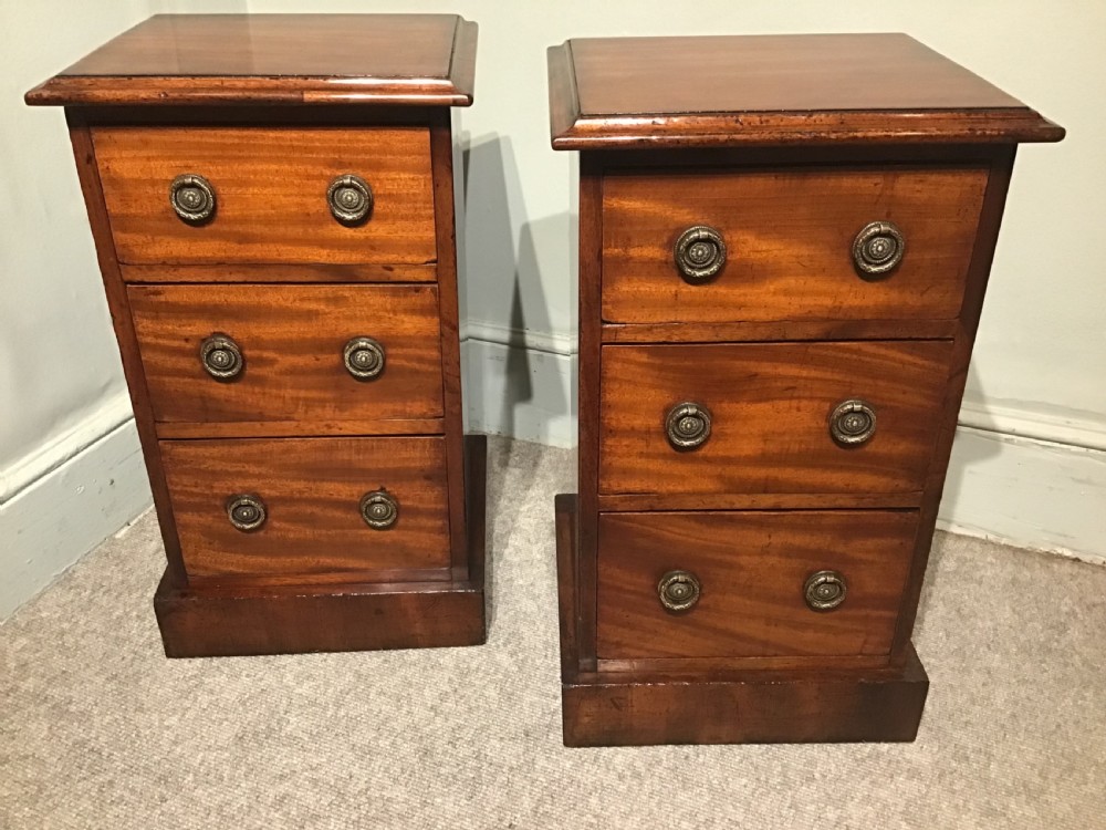 A pair of narrow antique mahogany bedside chests, each featuring three drawers with round brass ring handles and a plinth base. View IV