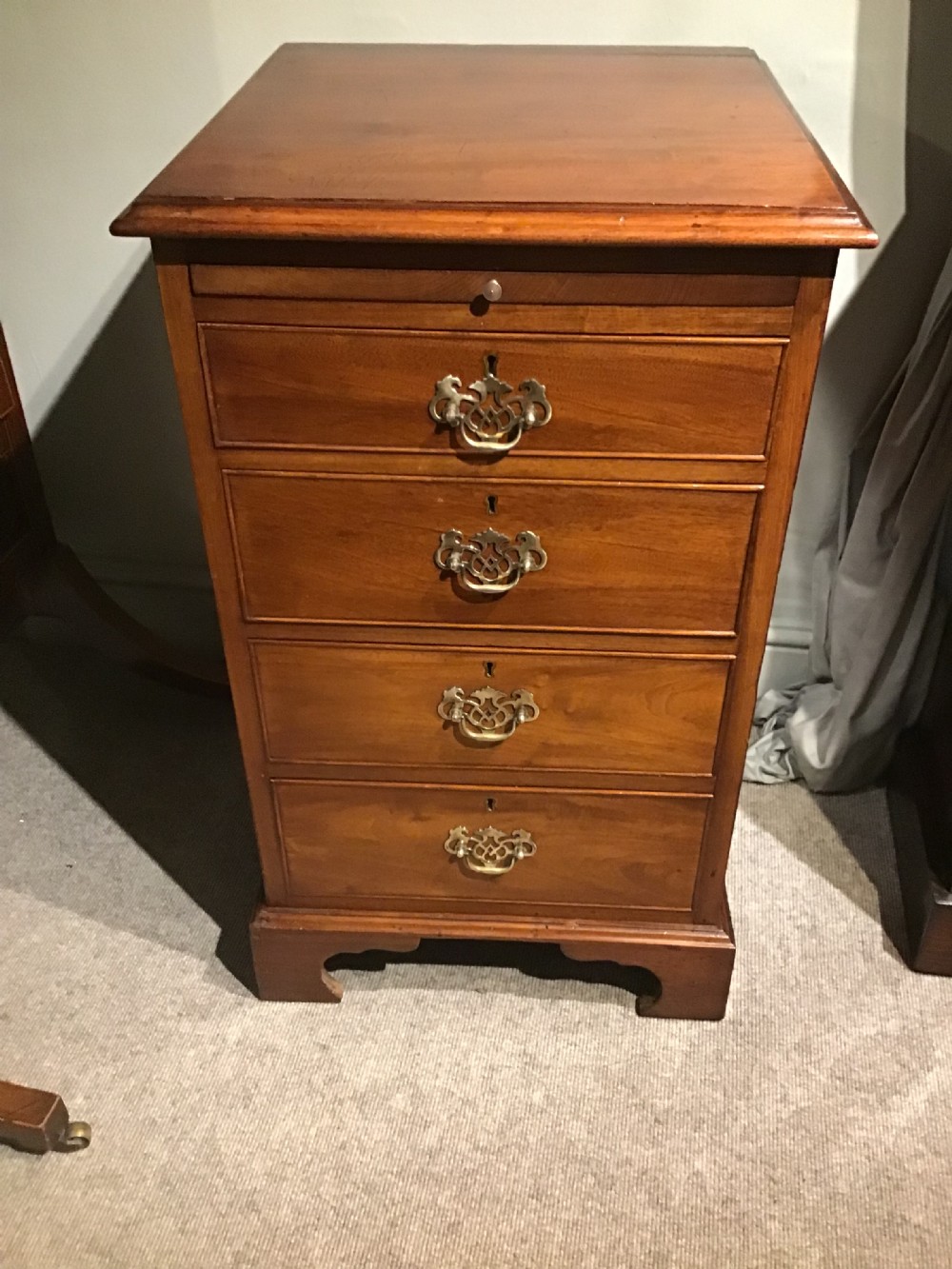 A narrow Georgian-style warm brown mahogany chest of drawers featuring four graduated drawers with pierced brass handles, a brushing slide, and bracket feet. View II