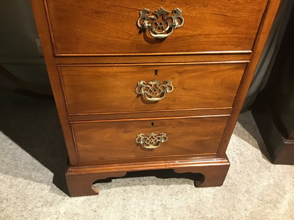 A narrow Georgian-style warm brown mahogany chest of drawers featuring four graduated drawers with pierced brass handles, a brushing slide, and bracket feet. View IV