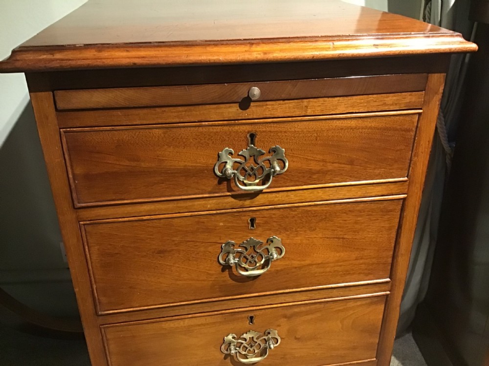 A narrow Georgian-style warm brown mahogany chest of drawers featuring four graduated drawers with pierced brass handles, a brushing slide, and bracket feet. View V