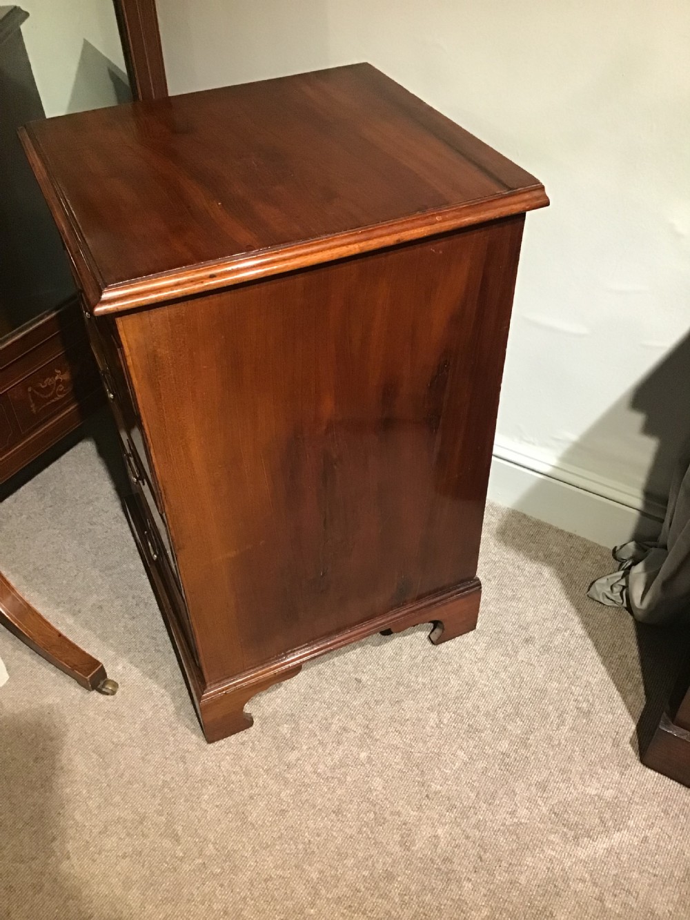 A narrow Georgian-style warm brown mahogany chest of drawers featuring four graduated drawers with pierced brass handles, a brushing slide, and bracket feet. View VI
