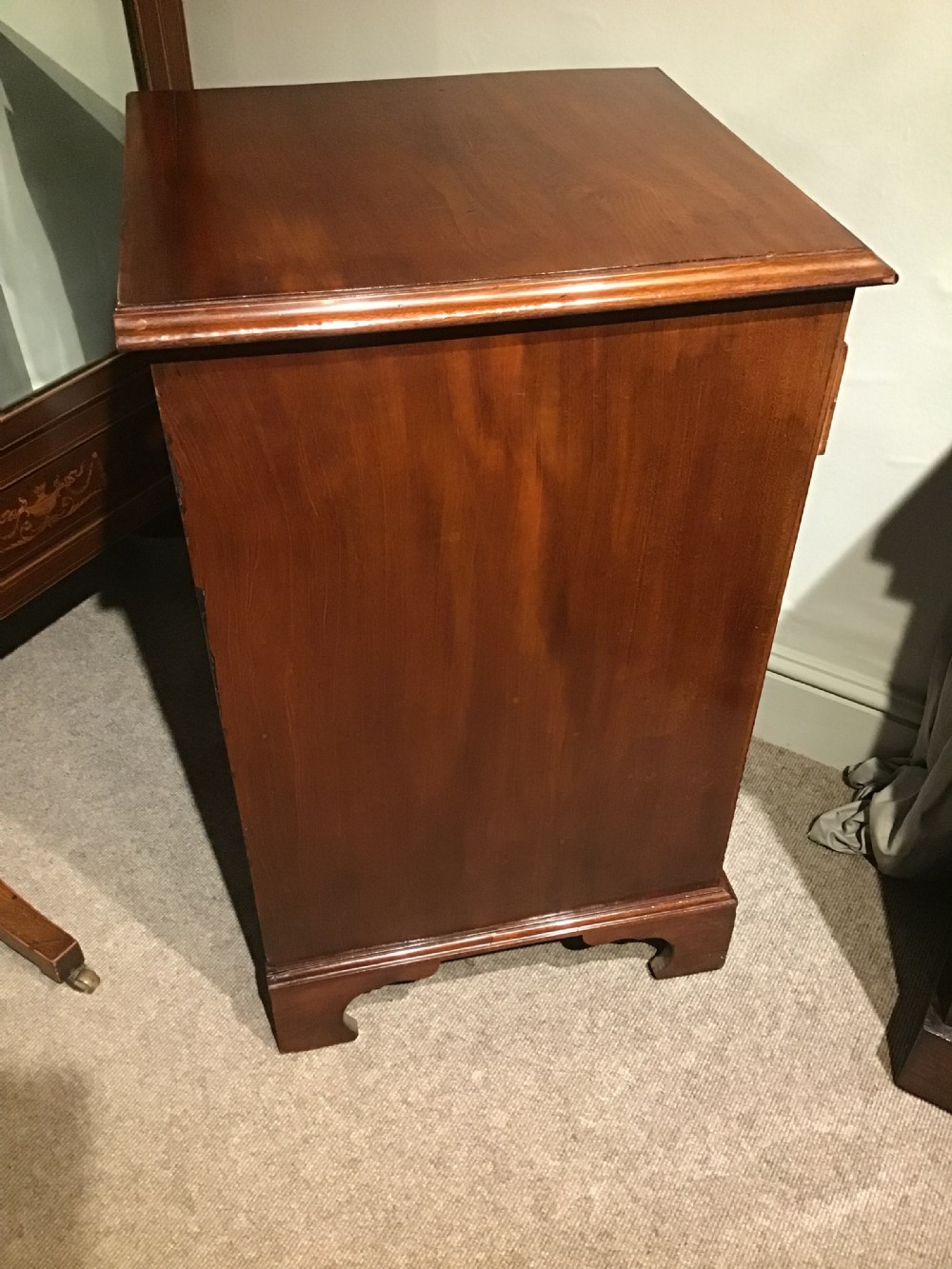 A narrow Georgian-style warm brown mahogany chest of drawers featuring four graduated drawers with pierced brass handles, a brushing slide, and bracket feet. View VII