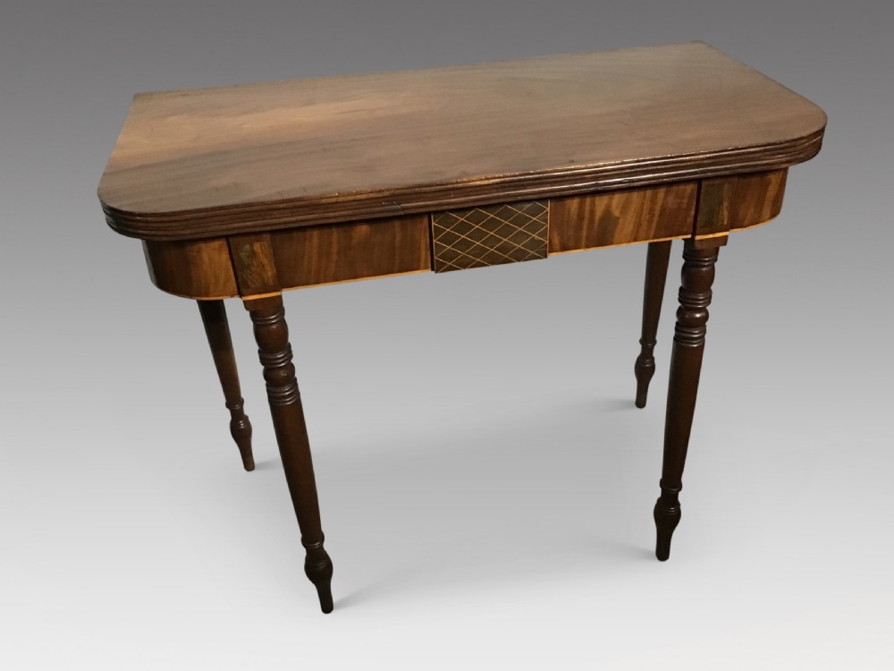 An antique dark mahogany fold-over tea table featuring turned legs and a central inlaid geometric motif on the front apron.