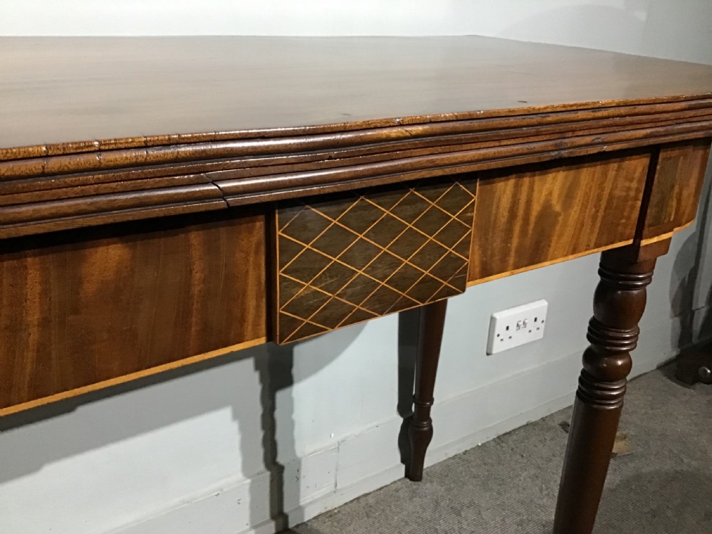 An antique dark mahogany fold-over tea table featuring turned legs and a central inlaid geometric motif on the front apron. View IV