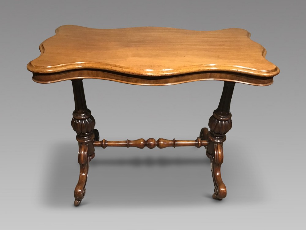 A Victorian mahogany side table featuring a serpentine-shaped top supported by carved baluster pedestals and a turned stretcher.