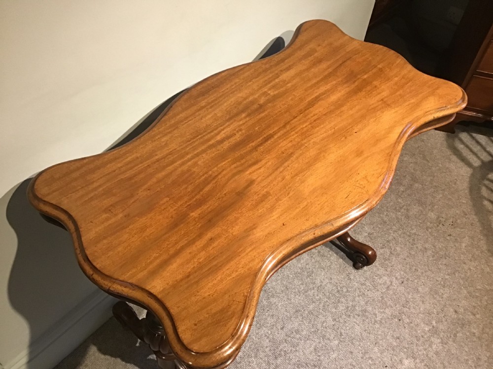A Victorian mahogany side table featuring a serpentine-shaped top supported by carved baluster pedestals and a turned stretcher. View II