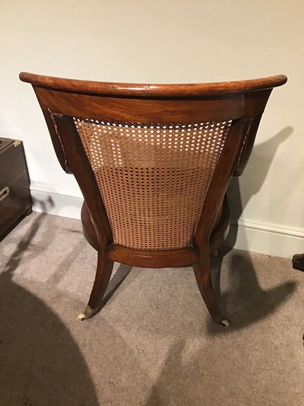A Regency mahogany bergere armchair featuring hand-woven cane panels, reeded turned front legs on brass castors, and a buttoned green velvet seat cushion. View III