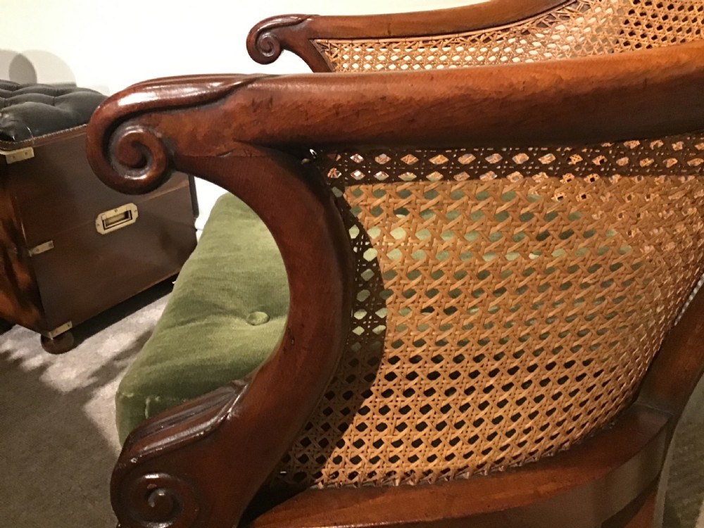 A Regency mahogany bergere armchair featuring hand-woven cane panels, reeded turned front legs on brass castors, and a buttoned green velvet seat cushion. View VII