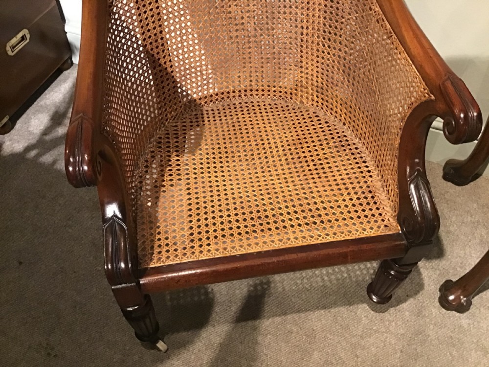 A Regency mahogany bergere armchair featuring hand-woven cane panels, reeded turned front legs on brass castors, and a buttoned green velvet seat cushion. View XIII