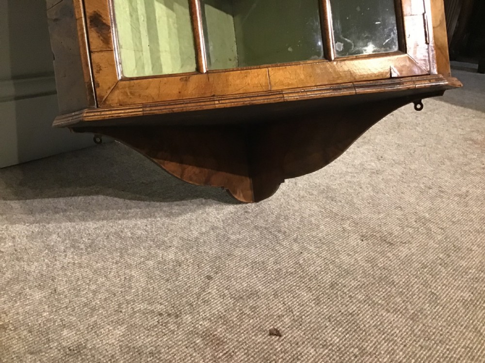 An antique walnut wall-hanging corner cabinet featuring an arched moulded pediment, glazed door with glass panes, and a green-painted interior with shelves. View III