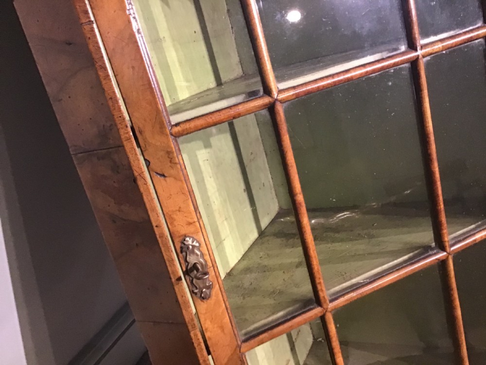 An antique walnut wall-hanging corner cabinet featuring an arched moulded pediment, glazed door with glass panes, and a green-painted interior with shelves. View V