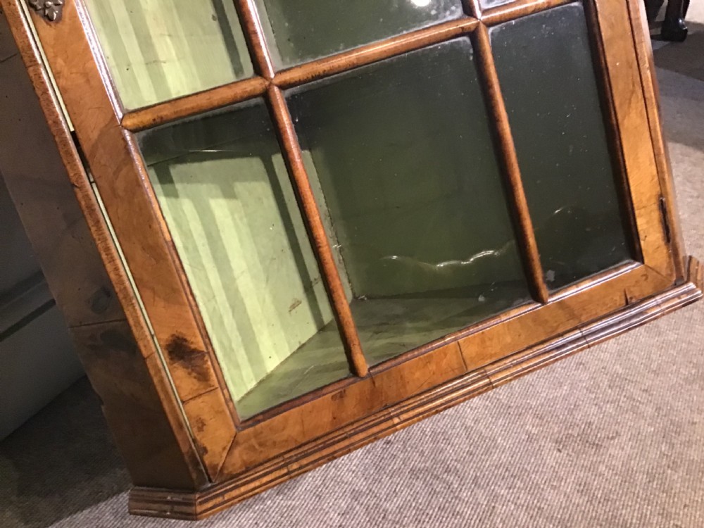 An antique walnut wall-hanging corner cabinet featuring an arched moulded pediment, glazed door with glass panes, and a green-painted interior with shelves. View VI