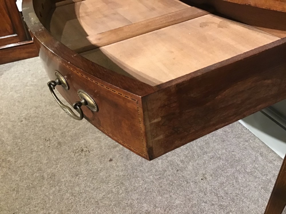 An antique oval mahogany writing table featuring a green leather top with gold tooling, a frieze drawer, and square tapered legs on brass castors. View IX