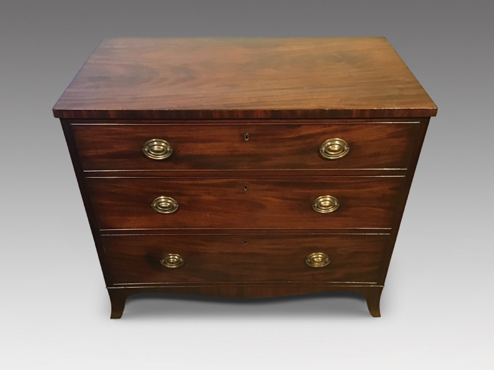 An antique mahogany chest of drawers featuring three drawers with brass oval handles and bracket feet.