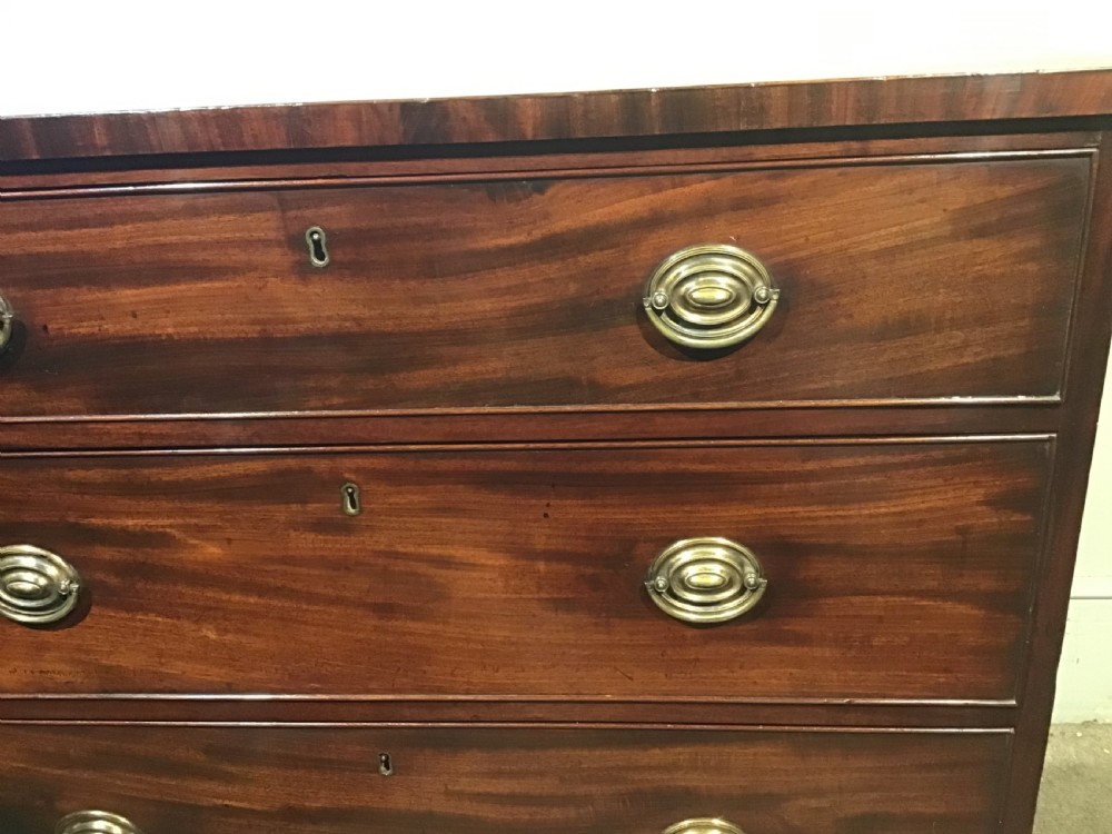 An antique mahogany chest of drawers featuring three drawers with brass oval handles and bracket feet. View V