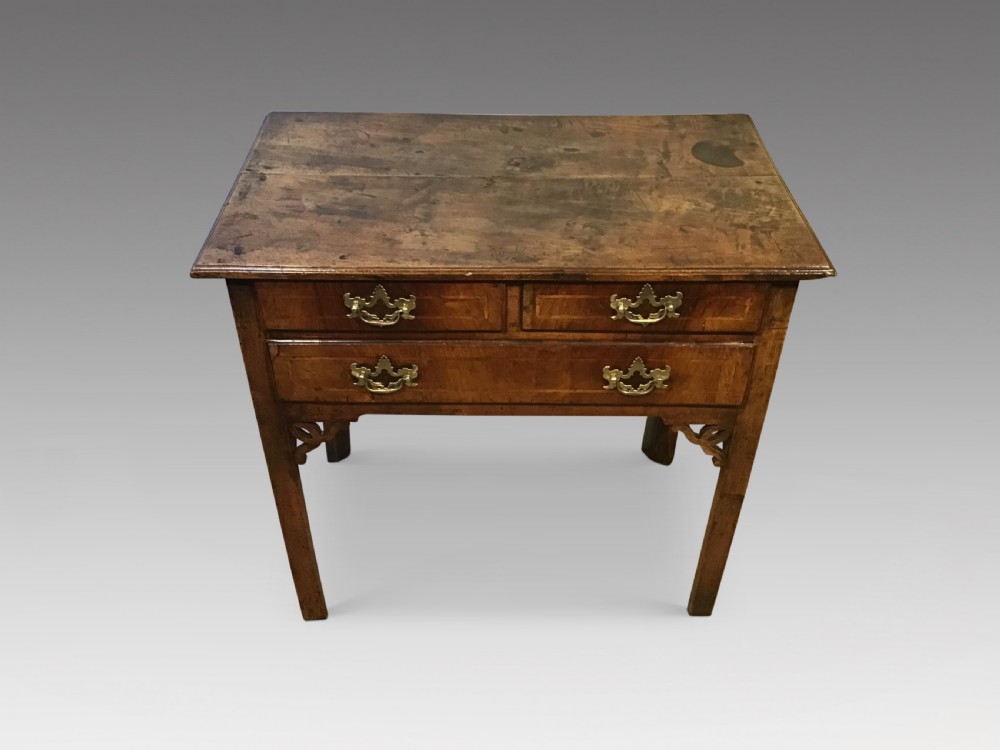 An 18th-century style antique walnut lowboy table featuring three drawers with decorative brass handles and fretwork corner brackets.
