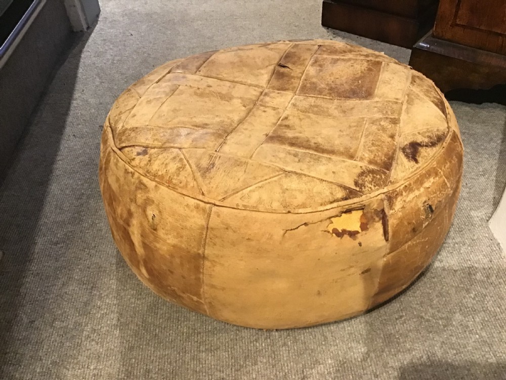 A circular low leather pouffe crafted from stitched tan panels showing patinated surface wear. View II