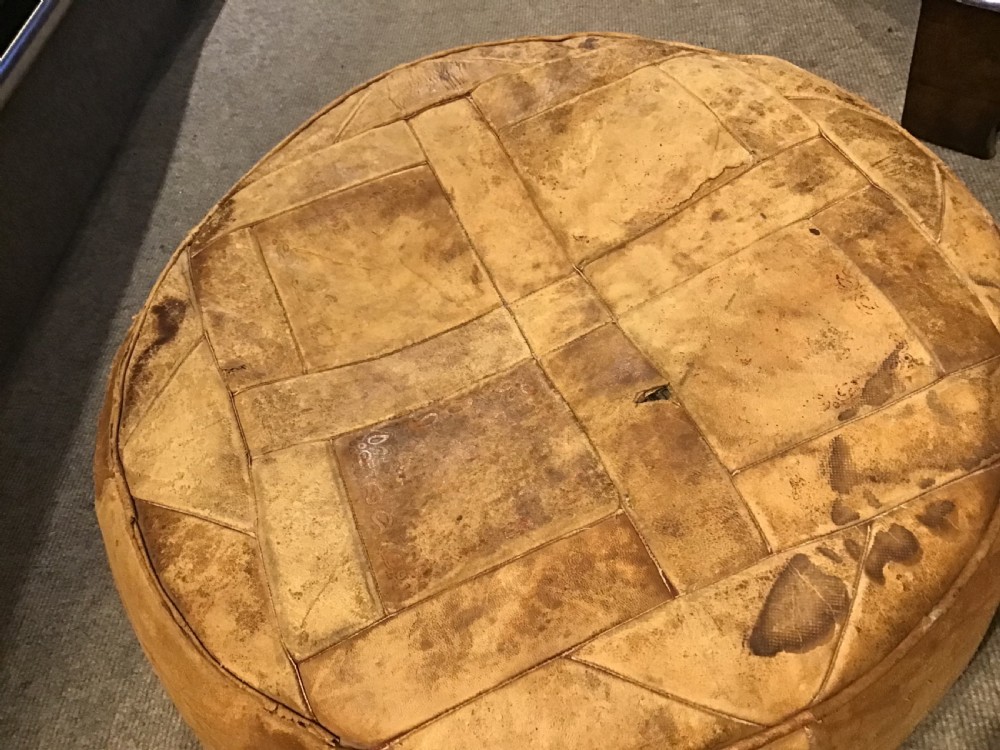 A circular low leather pouffe crafted from stitched tan panels showing patinated surface wear. View III