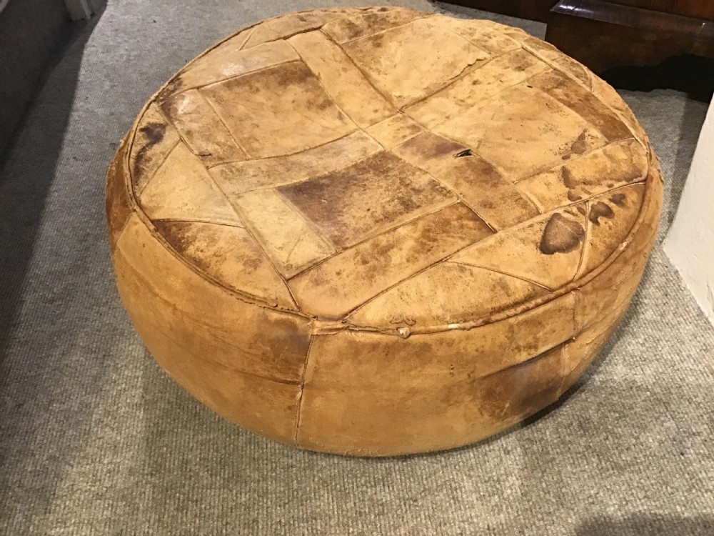 A circular low leather pouffe crafted from stitched tan panels showing patinated surface wear. View IV