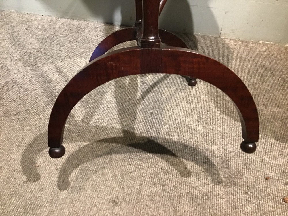 An antique dark mahogany folding occasional table featuring a round top, lower semi-circular shelf, turned uprights, and curved feet. View V