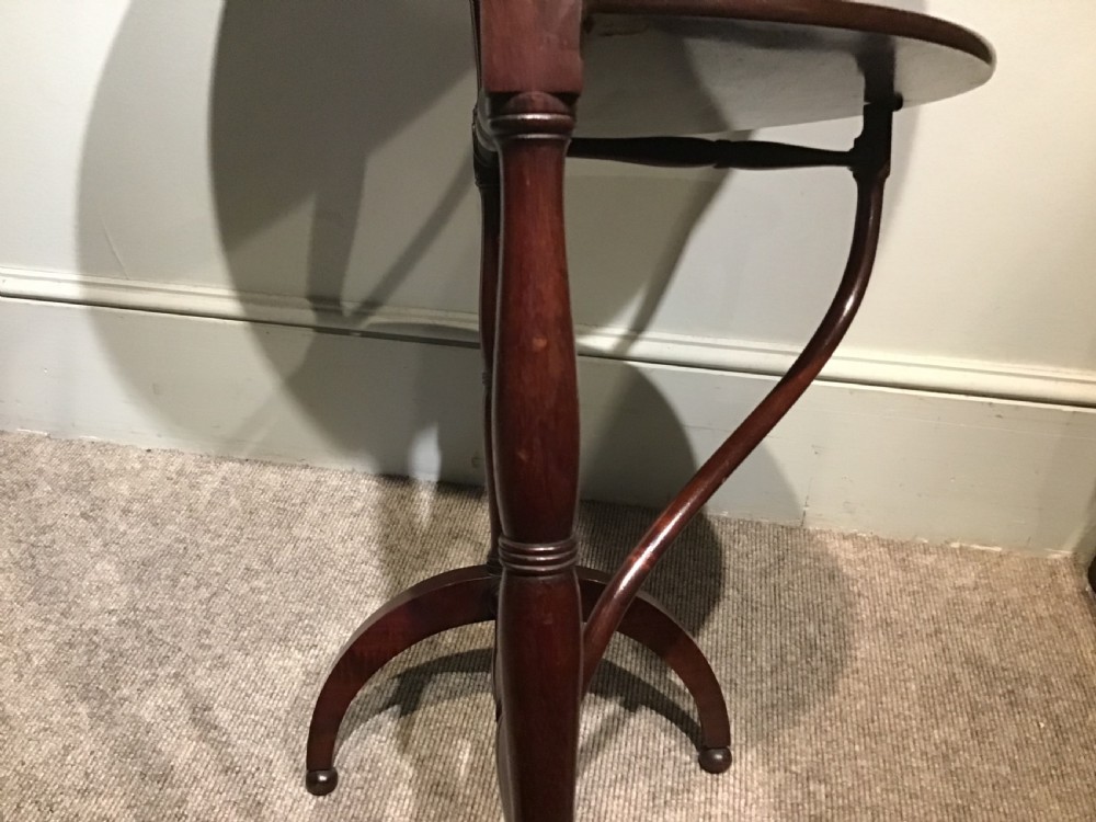 An antique dark mahogany folding occasional table featuring a round top, lower semi-circular shelf, turned uprights, and curved feet. View VI
