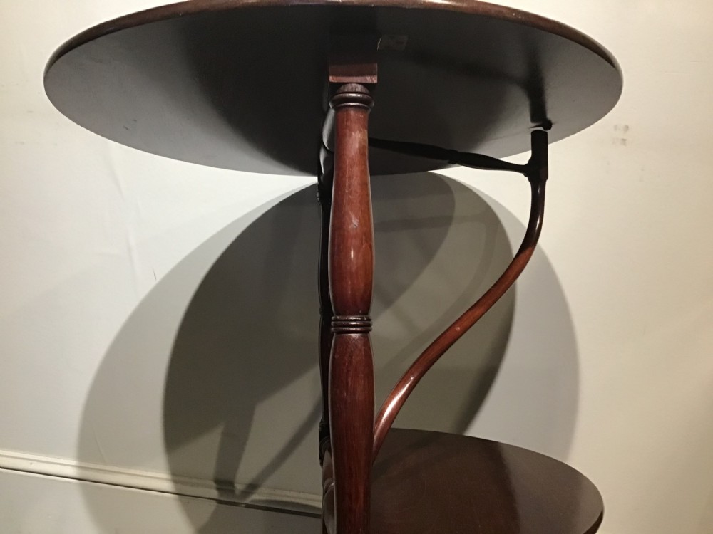 An antique dark mahogany folding occasional table featuring a round top, lower semi-circular shelf, turned uprights, and curved feet. View VII
