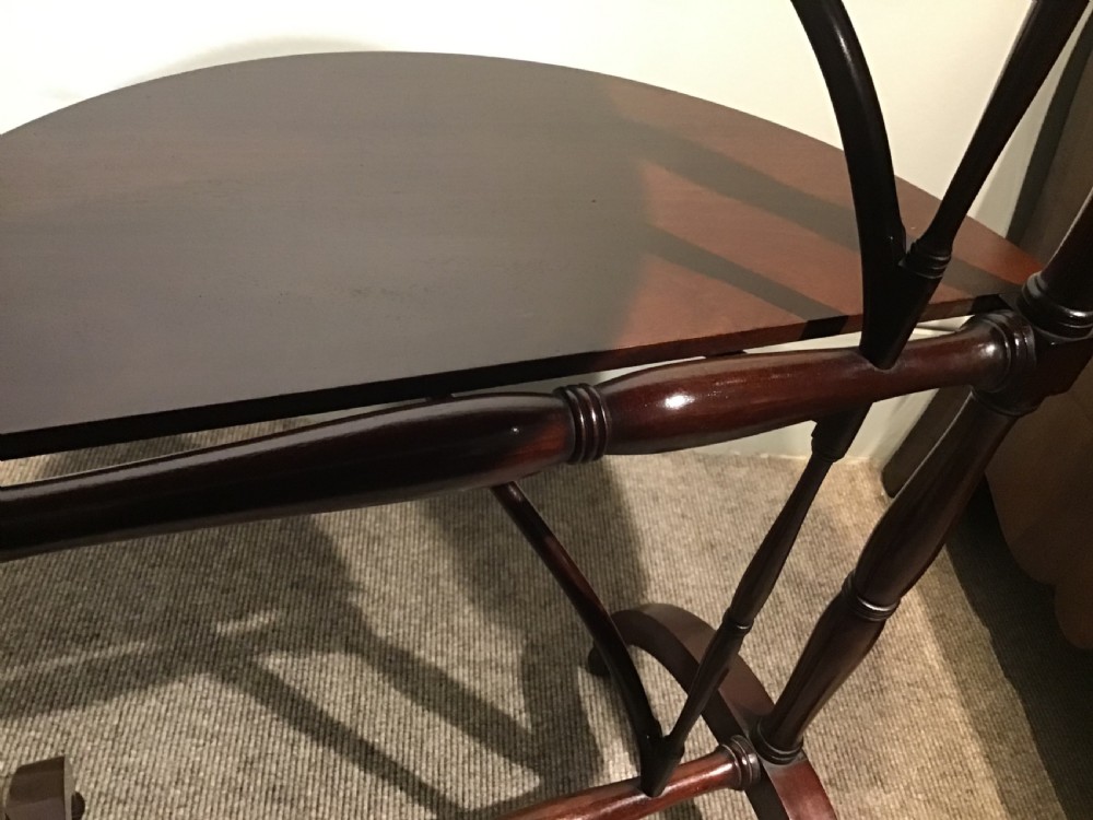 An antique dark mahogany folding occasional table featuring a round top, lower semi-circular shelf, turned uprights, and curved feet. View X