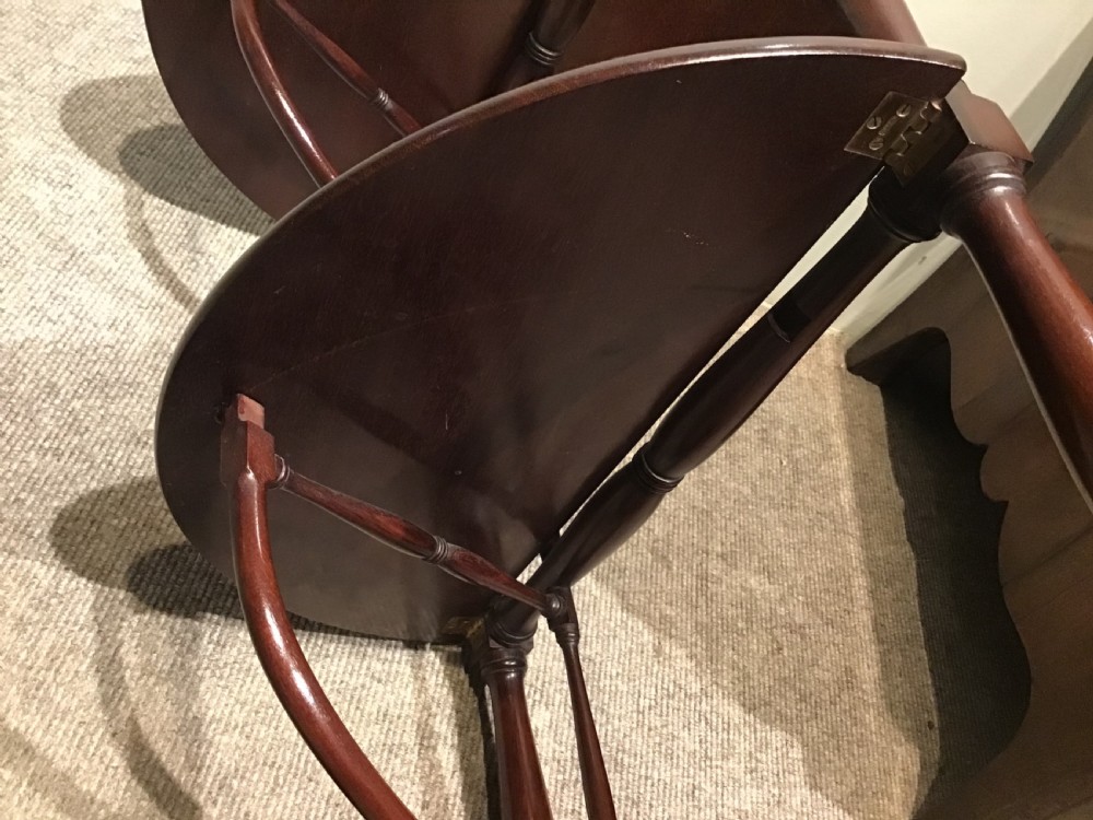 An antique dark mahogany folding occasional table featuring a round top, lower semi-circular shelf, turned uprights, and curved feet. View XI