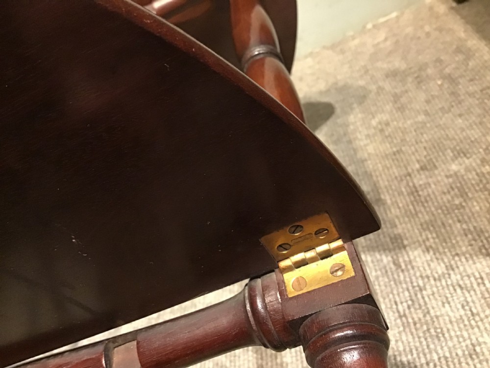 An antique dark mahogany folding occasional table featuring a round top, lower semi-circular shelf, turned uprights, and curved feet. View XV