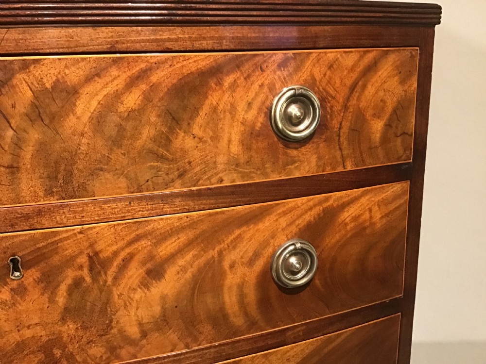 A mahogany bow-front chest of drawers featuring four graduated drawers with flame veneers, brass ring handles, and splayed bracket feet. View II