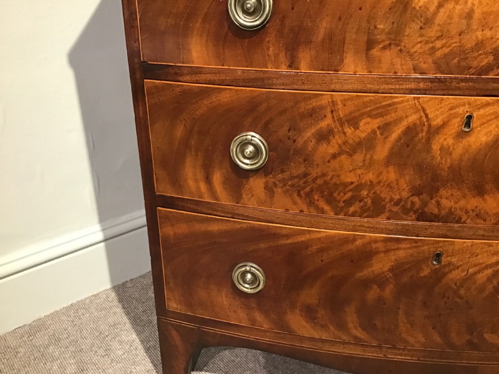 A mahogany bow-front chest of drawers featuring four graduated drawers with flame veneers, brass ring handles, and splayed bracket feet. View III