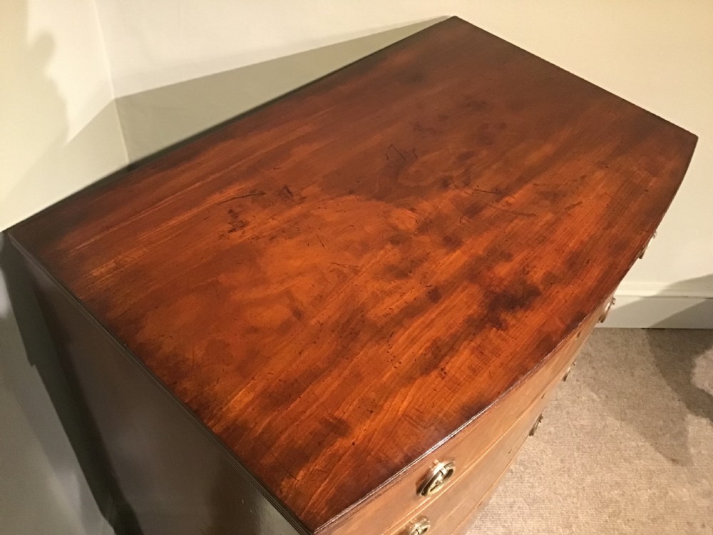 A mahogany bow-front chest of drawers featuring four graduated drawers with flame veneers, brass ring handles, and splayed bracket feet. View VI