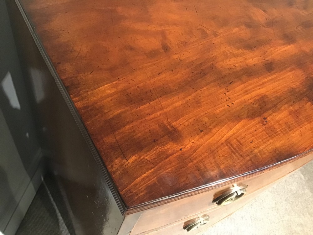 A mahogany bow-front chest of drawers featuring four graduated drawers with flame veneers, brass ring handles, and splayed bracket feet. View VII