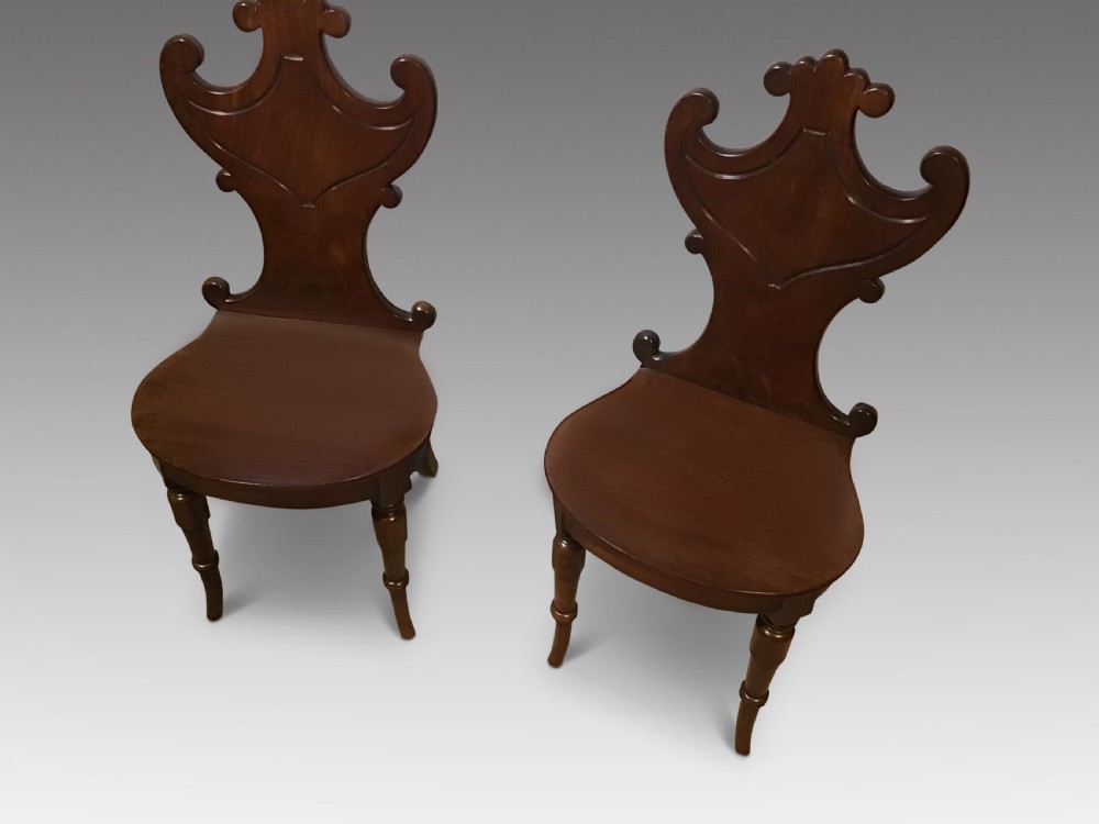 A pair of antique dark mahogany hall chairs featuring carved scroll backs, solid wood seats, and turned front legs. View II